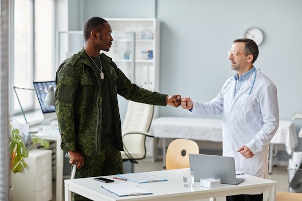 African American army officer leaning on walking stick greeting mature Caucasian doctor with fist bump